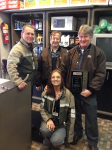 AFM Phil McGonagle (left) and MCP Sandie Gardner (kneeling) present a 60-year U-Haul plaque to Brian Bearde (right) and his longtime employee Jack Pagnano (center).